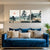 Blue sofa with decorative pillows in a living room with wall art depicting trees and mountains.