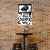 Brick wall with a framed poster of a vintage car and text, below a wooden table and stools.