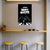 Poster with black and white design on a wall above a wooden shelf with stools below.