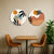 Two circular wall art pieces on a beige wall above a wooden table with two chairs.