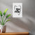 White wall with a tooth-shaped poster featuring black text, next to a potted plant on a wooden surface.
